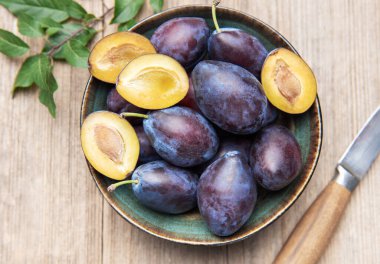 Plums filling a ceramic bowl, some cut open, on a light wooden background