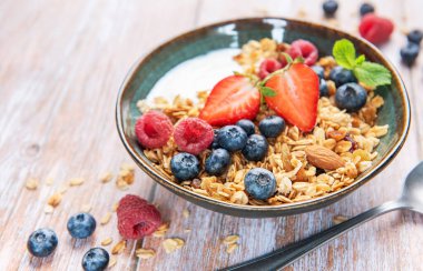 Granola with yogurt, strawberries, blueberries, and raspberries in a ceramic bowl