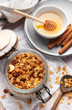 Granola in a glass jar with honey and cinnamon sticks on a light wooden background