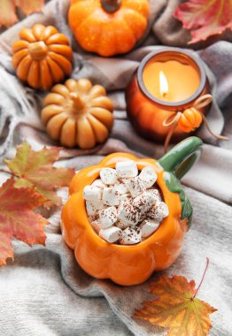 Sıcak kakaolu balkabağı kupası ve sonbahar yapraklı ve mumlu rahat bir battaniyede marşmelov.