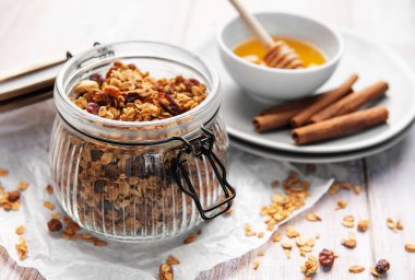 Granola with oats, nuts, and dried fruit in a jar, with honey and cinnamon
