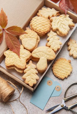 Ev yapımı sonbahar temalı kurabiyeler, bir kutuda ip, etiket ve dökülen yapraklar hediye için hazırlanıyor.