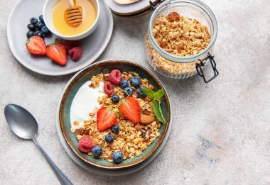 Granola bowl with yogurt, strawberries, blueberries, raspberries, mint, and almonds on a grey background