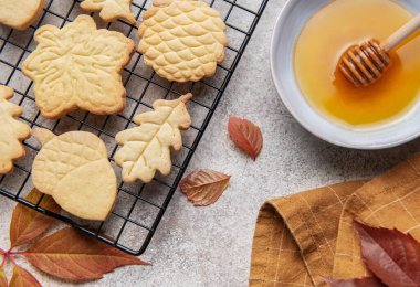 Taze pişmiş kurabiyeler tel askıda soğuyor. Bir kase bal ve sonbahar yapraklarının yanında.