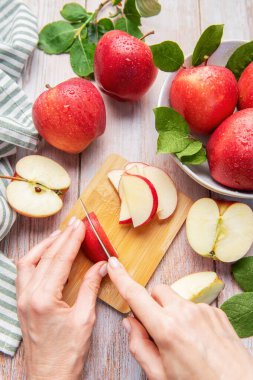 Hands slicing a red apple on a wooden cutting board with more fresh apples around