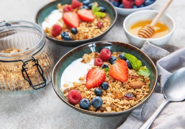 Sağlıklı bir kahvaltı için taze çilek, yabanmersini, ahududu, yoğurt, fındık ve bal dolu granola kaseleri.