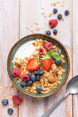 Granola with yogurt, strawberries, blueberries, and raspberries in a ceramic bowl