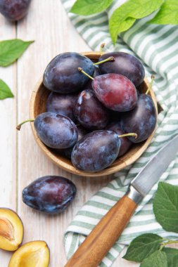 Juicy ripe plums in a bowl, one sliced, with a knife on a striped napkin