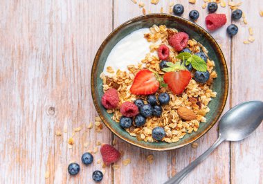 Granola with yogurt, strawberries, blueberries, and raspberries in a ceramic bowl