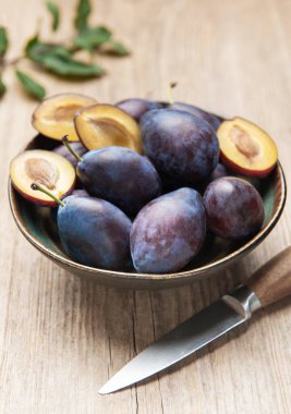 Plums filling a ceramic bowl, some cut open, on a light wooden background