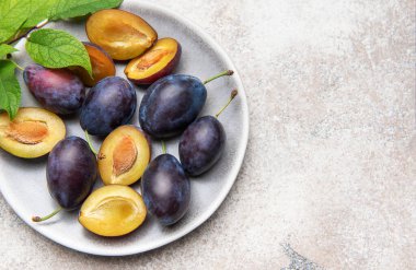 Beyaz seramik tabakta yeşil yapraklı olgun mor ve sarı erikler.