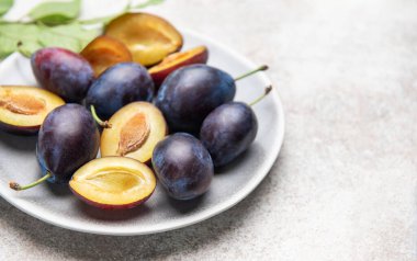 Beyaz seramik tabakta yeşil yapraklı olgun mor ve sarı erikler.