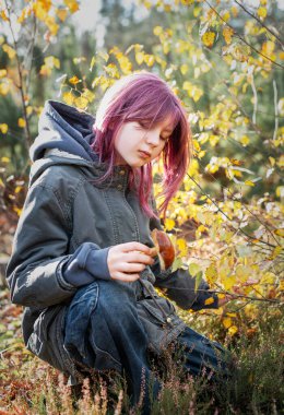 Genç bir dişi diz çöküp, canlı bir ormanda bulunan mantarı tutuyor.