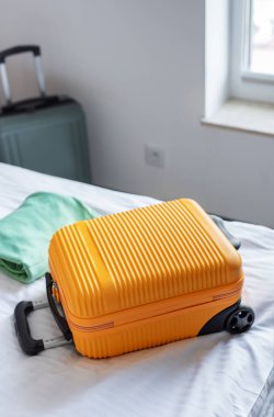 Sarı bavul ikinci bir çanta ile bir yatakta, seyahat hazırlığını ve ayrılışı sembolize ediyor