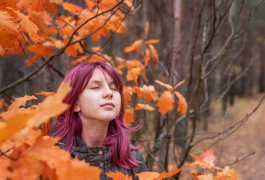 Güz ormanında canlı portakal yaprakları arasında taze hava soluyan rahatlatıcı kız.