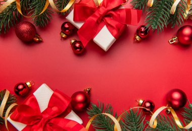 Noel hediyeleri, köknar dalları ve kırmızı süsler kırmızı arka planda şenlikli bir sınır oluşturuyor.