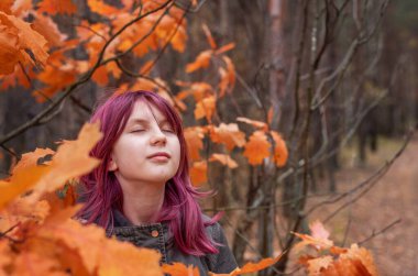Güz ormanında canlı portakal yaprakları arasında taze hava soluyan rahatlatıcı kız.