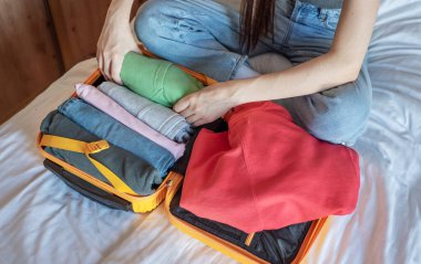 Giysileri turuncu bir bavula saran, seyahat için hazırlanan bir kadın.