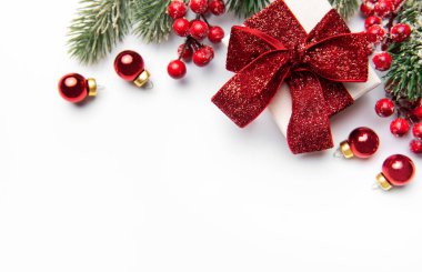 Beyaz arka planda parlak kırmızı bir fiyonk, kutsal böğürtlen ve takılar olan bir hediye kutusu.