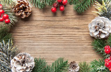 Evergreen dalları, kırmızı böğürtlenler ve kozalaklar ahşap bir yüzey etrafında şenlikli bir sınır oluşturuyor.