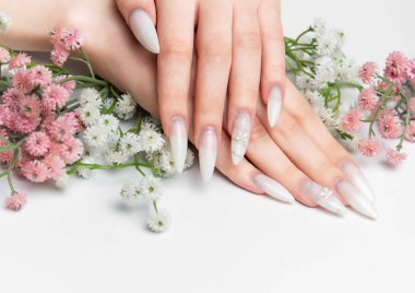 Beyaz arka planda çiçekli zarif beyaz ombre tırnaklar sergiliyor.