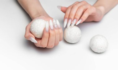 Kadın elleri parıltılı toplarla güzel beyaz manikür yapıyor.