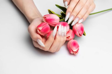 Beyaz topuklu tırnaklı kadın elleri kapalı pembe lale buketi tutuyor.