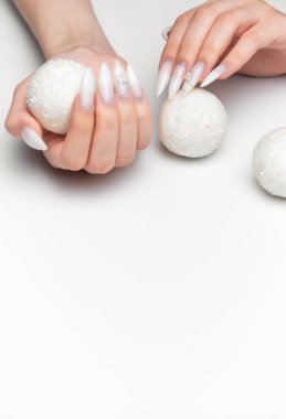 Manikürlü, uzun beyaz tırnaklı, beyaz arka planda dekoratif parıltılı toplar tutan kadın elleri.