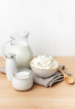 Ahşap tezgahta çeşitli taze süt ürünleri ve arka planda beyaz fayanslar var.