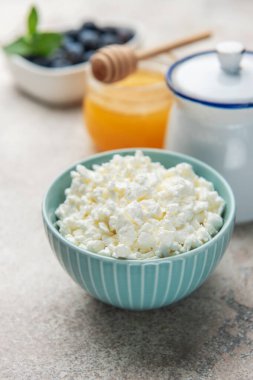 Sağlıklı bir kahvaltı için bal, yabanmersini ve nane aromalı mavi bir kasede süzme peynir.