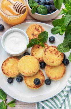 Syrniki, bir tabak geleneksel süzme peynirli krep, yabanmersini, taze nane, ekşi krema ve bal ile servis edilir.