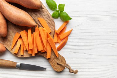 Bıçak ve taze fesleğenle dilimleme tahtasının üzerinde çiğ patates kızartması hazırlıyorum.