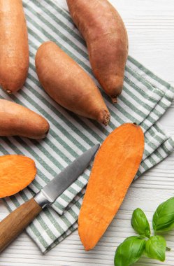 Çizgili kumaş üzerinde tatlı patates, bıçak ve fesleğen, sağlıklı vejetaryen yemekleri hazırlıyor.