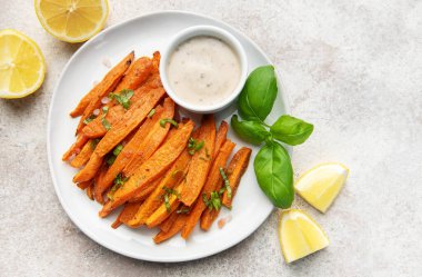 Taze fesleğenli patates kızartması ve beyaz tabakta limon dilimleri.