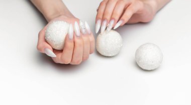 Kadın elleri parıltılı toplarla güzel beyaz manikür yapıyor.