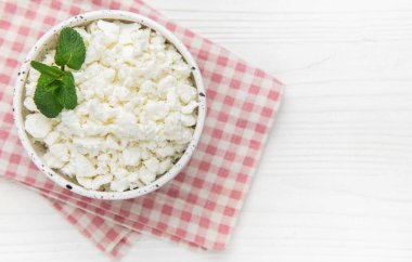 Ekose peçetede nane yaprakları olan seramik bir kasede süzme peynir.