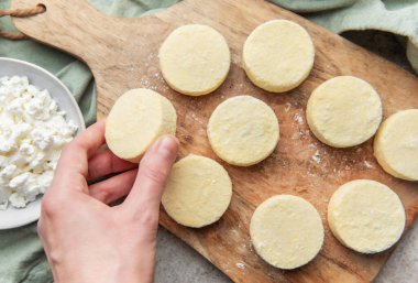 Hand placing raw syrniki pancakes made from quark on a wooden board for cooking