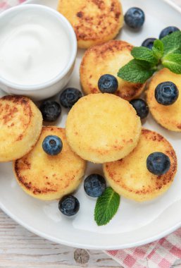 Syrniki, yaban mersini ve nane yaprakları ekşi kremalı beyaz bir tabakta.