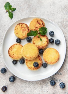 Golden brown syrniki pancakes served with fresh blueberries and a mint sprig on a white plate