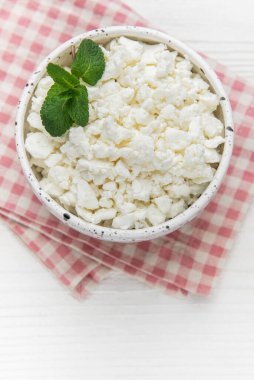 Kırmızı gingham peçetedeki nane yapraklarıyla süslenmiş taze süzme peynir bir kâseyi dolduruyor.