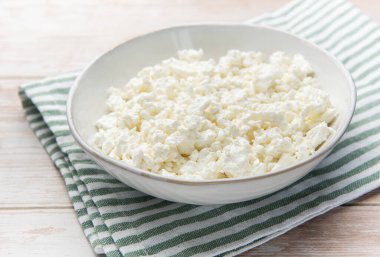 Yeşil çizgili bir peçetenin üzerinde beyaz bir kasede duran süzme peynir.