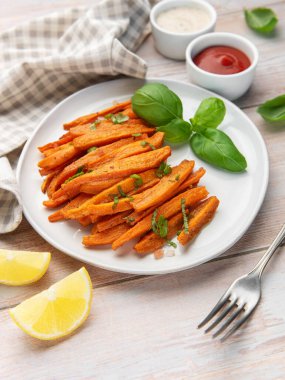 Beyaz bir tabakta taze fesleğen, limon ve sos ile servis edilen patates kızartması.