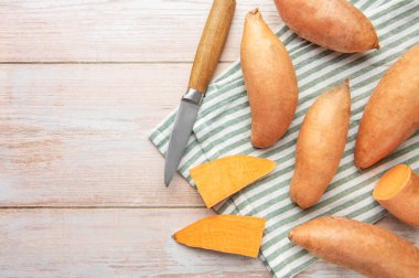 Tahta masadaki tatlı patates, bıçak ve çay havlusu sağlıklı yiyecekler hazırlıyor.