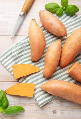 Tahta masadaki tatlı patates, bıçak ve çay havlusu sağlıklı yiyecekler hazırlıyor.