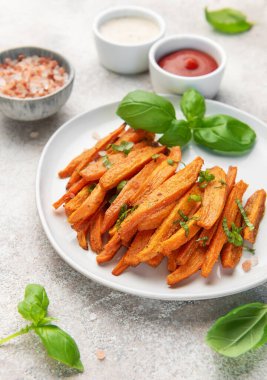 Fesleğenli ve soslu beyaz tabakta servis edilen patates kızartmaları.