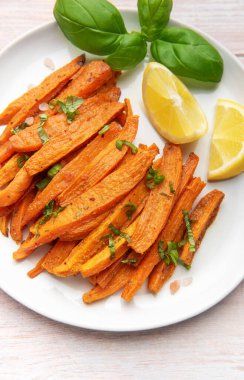 Beyaz bir tabakta taze fesleğen ve limon dilimleri ile servis edilen patates kızartmaları.