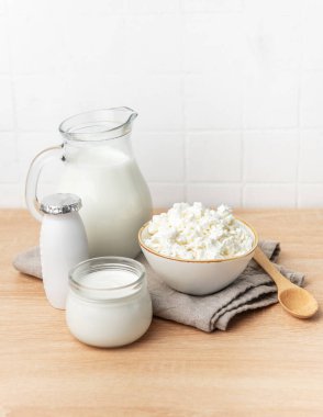 Ahşap tezgahta çeşitli taze süt ürünleri ve arka planda beyaz fayanslar var.
