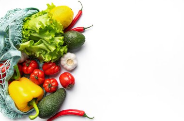 Taze organik sebzeler ve meyveler beyaz arka planda yeniden kullanılabilir sicim torbasından fışkırıyor.