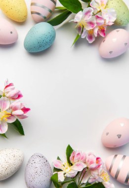 Pastel renkli paskalya yumurtaları. Beyaz bir yüzeyde çiçek açan elma çiçekleri.