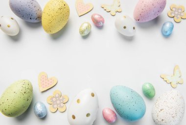 Şenlikli pastel benekli yumurtalar, tahta kalpler ve kelebekler neşeli bir bahar sınırı oluşturuyor.